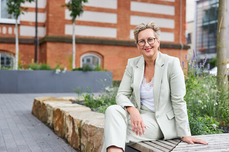 A woman in a green blazer sits outside in front of a building and laughs __A woman in a green blazer sits outside in front of a building and laughs