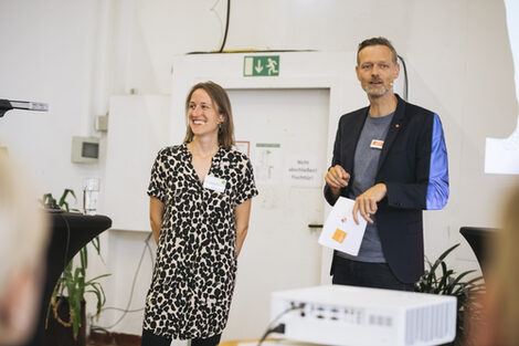 Zwei Personen stehen vor einem Publikum.