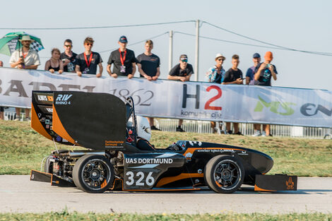 Der Rennwagen der FH auf der Stecke. Menschen schauen zu.