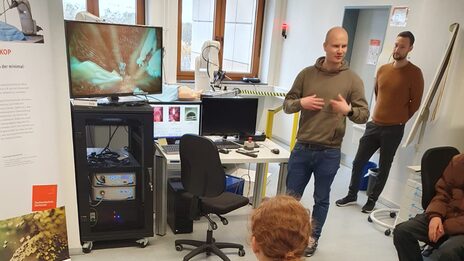 A group of pupils listens to a presentation by a member of staff in the laboratory.