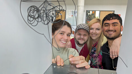 Four people look through a metal box in which they have hung their wire construction.