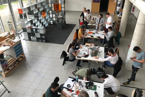 In the foyer of the architecture, several people work together in groups at different tables.