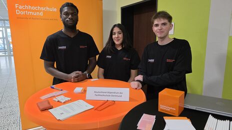 Drei Personen stehen hinter einem Tisch mit verschiedenen Utensilien.