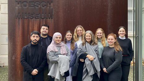 Group of students with Professor Diana Reichle in front of the entrance sign to the Hoesch Museum.