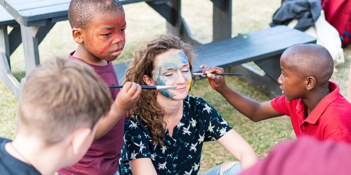 A student's face is painted with brushes by children in South Africa.