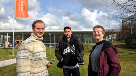 Drei Personen stehen auf einer Wiese auf dem FH-Campus an der Emil-Figge-Straße und sprechen miteinander.