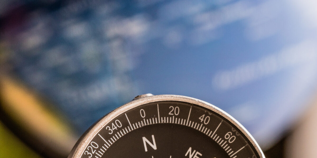 Photo of a compass, in the background a very blurred globe.