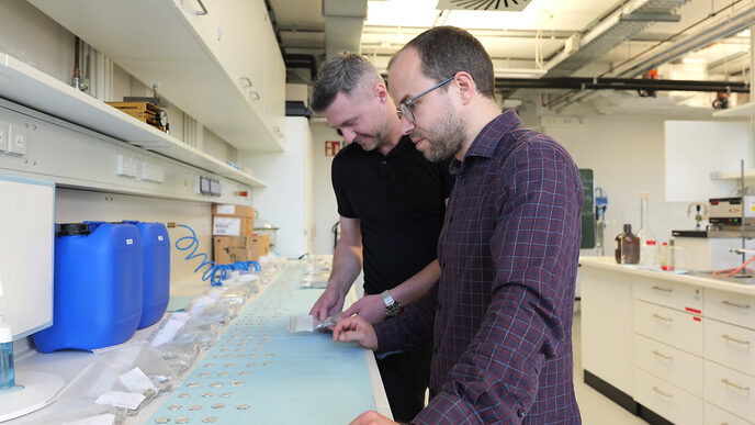 Two people are standing in a laboratory analyzing samples.