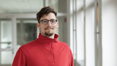 Eine Person im roten Pullover schaut freundlich in die Kamera.