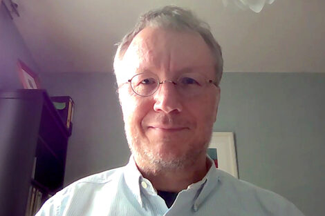 A man sits in front of a webcam in his home office.