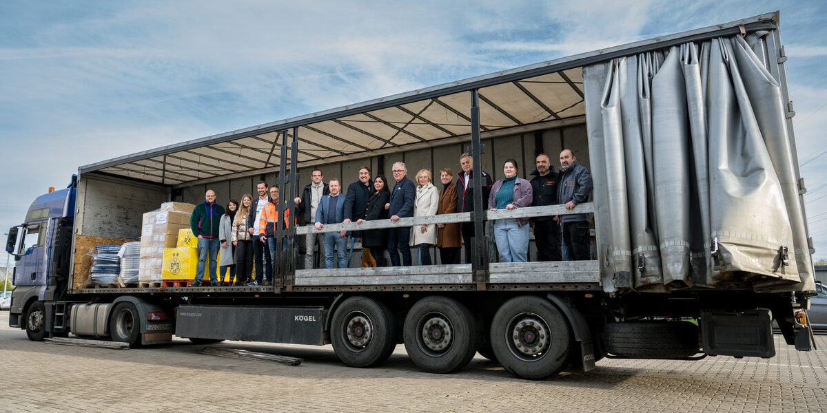 Several people are standing next to parcels on the loading area of a large truck.