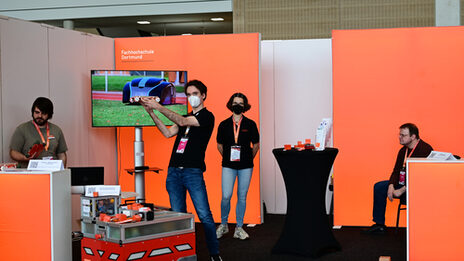 Messestand mit Robotern als Exponate; Fernseher zeigt Videos; Standmitarbeiter hält EduRob hoch