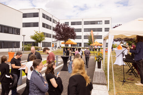 Impression des Sommerfests 2022. Menschen stehen auf dem Campus Emil-Figge-Straße an Stehtischen und unterhalten sich, während eine Liveband spielt.