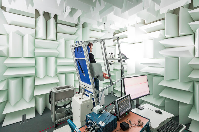 Photo of an experimental set-up for measuring blood pressure using a tilting table. A man is attached to the tilting table in a laboratory, which is almost vertical. Monitors and equipment are set up in front of it.