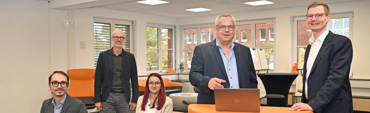 Eine Personengruppe steht und sitzt an und um einem orangefarbenen Pult im User Innovation Center.