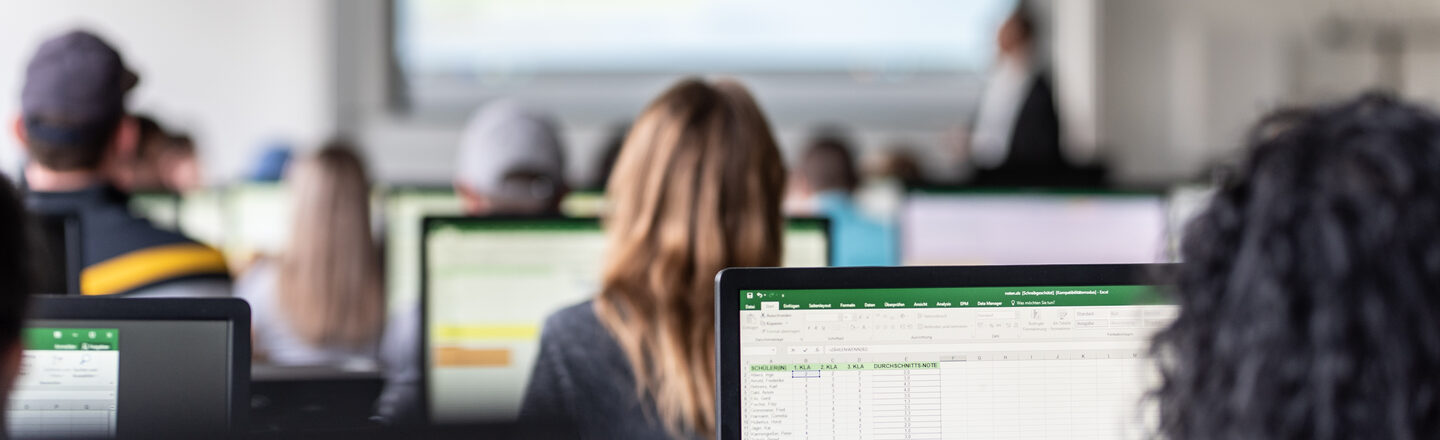 Blick von hinten in den Computerraum mit Studierenden, auf den Monitoren sind zum Teil Excel-Tabellen erkennbar.