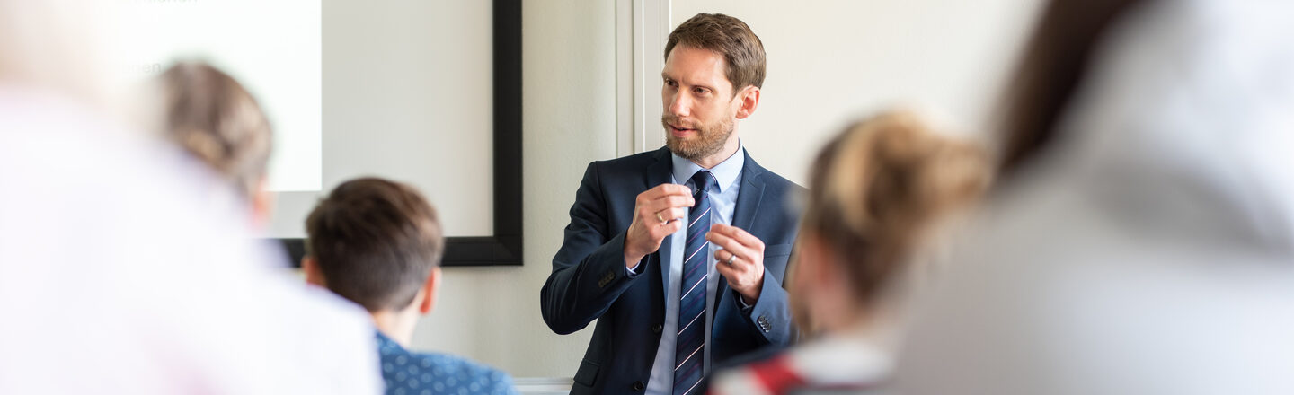 Photo of a teacher standing in front of his students and explaining something