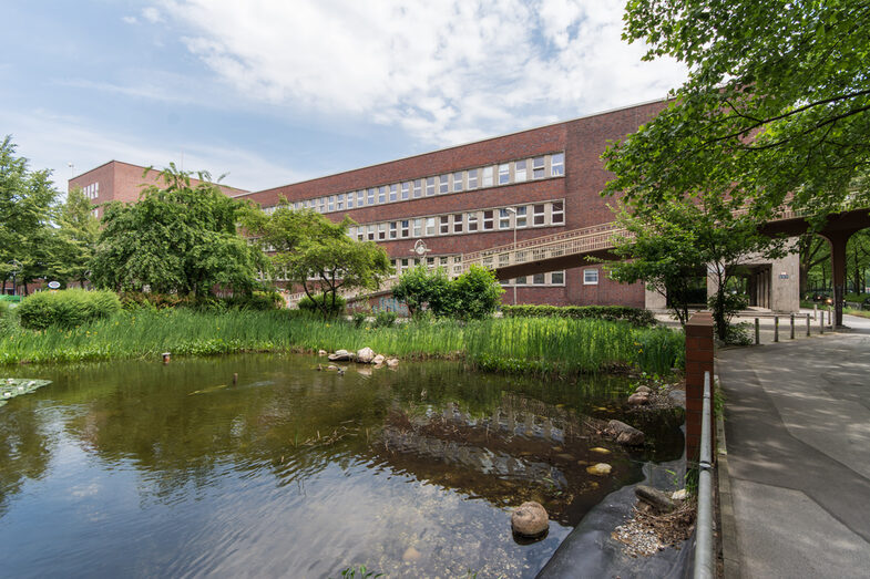 Photo with a view across a pond towards the Faculty of Design building on Max-Ophüls-Platz.