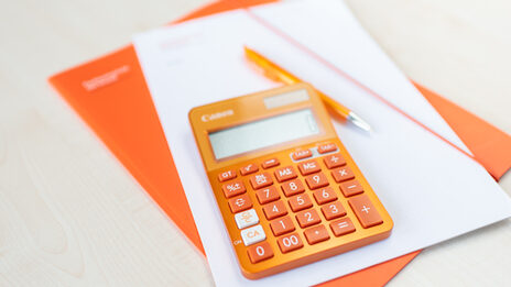 An orange calculator lies on an orange folder and a pile of notes.