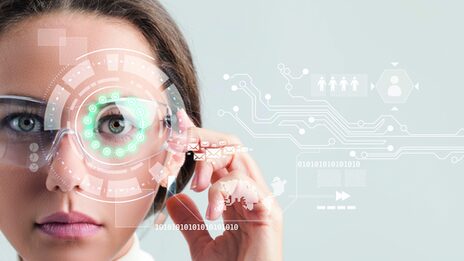 Portraitfoto einer Frau mit einer Brille mit Knopf an der Seite, auf den sie drückt. Um ihr linkes Auge herum sind Kreise und Formen animiert, links von ihr noch weitere Symbole.