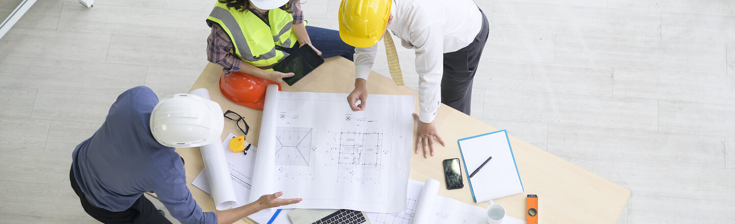 3 engineers in a meeting at a table with plans and end devices