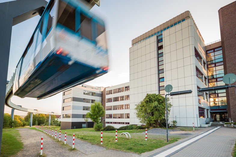 Photo of the building at Emil-Figge-Straße 44, with the H-Bahn tracks on the left and the H-Bahn passing by.