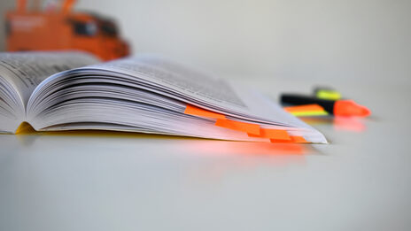 Photo of an open book with orange sticky notes inside. In the background is a pencil box and highlighters.