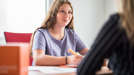 Photo of a student sitting opposite another woman, who can only be seen in the crop on the right of the picture. They are having a student counseling interview.